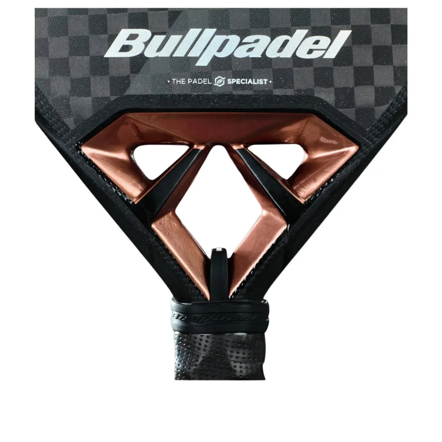 A close-up of the BULLPADEL RACKET VERTEX 04 2025 JUAN TELLO by Padel Smash Academy shows its carbon fiber design and geometric copper openings near the handle, a black wrapped grip, and The Padel Specialist logo for total game control.