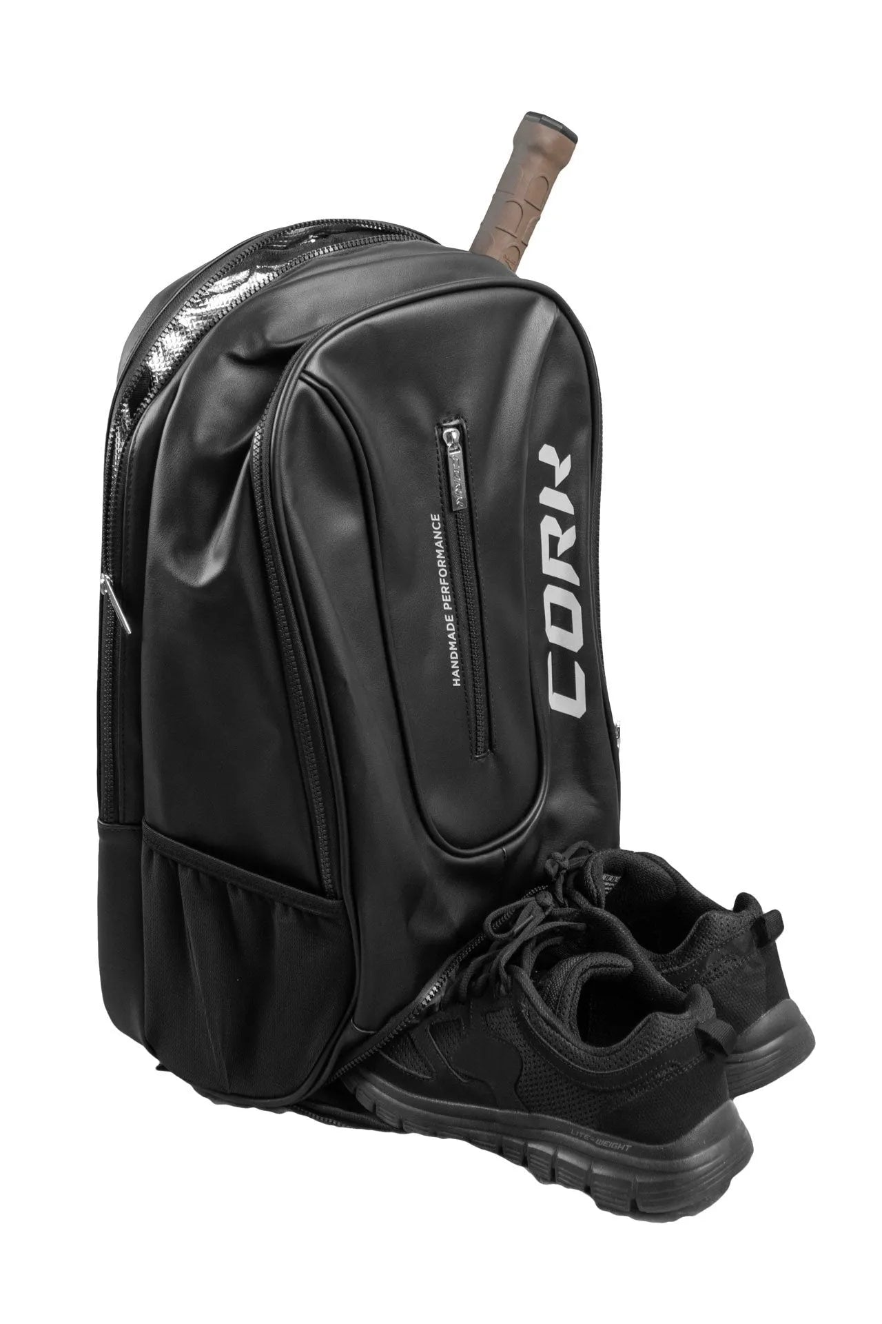A Cork Padel backpack in black, tailored with multiple compartments, zippers, and a thermal pocket for your essentials, with a pair of black athletic shoes and a tennis racket handle peeking out—ideal as a lightweight padel backpack.