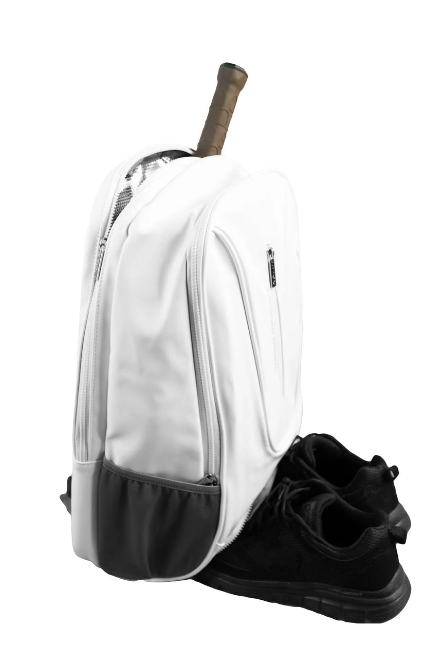The Cork Padel Backpack, by Cork Padel, in white with black trim, features a tennis racket handle sticking out and a thermal pocket for gear protection. A pair of black athletic shoes is placed slightly in front of the lightweight backpack.