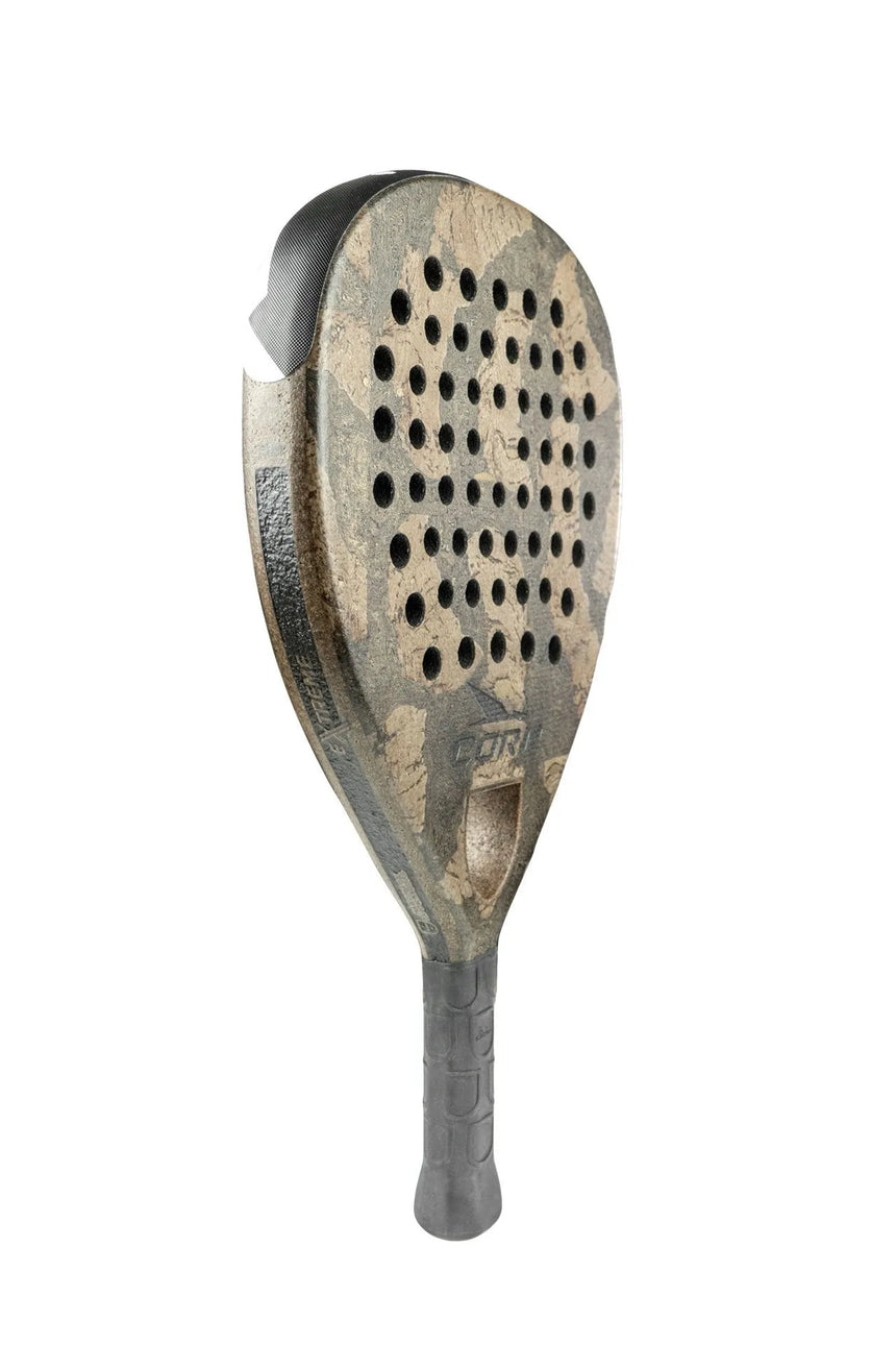 Close-up of the Cork Padel Extreme Black showcases its worn, textured surface. A creation by Cork Padel, it features multiple circular holes and a black handle with a patterned grip against a plain white background.