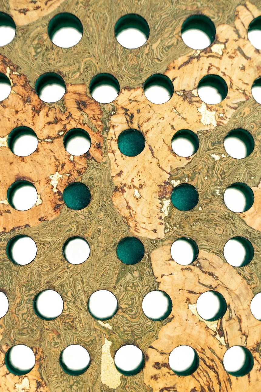 The Cork Padel Extreme Green by Cork Padel features a camouflage-like textured surface with earthy green and beige tones, characterized by multiple rows of round holes, each revealing a dark interior, reminiscent of a limited edition racket.