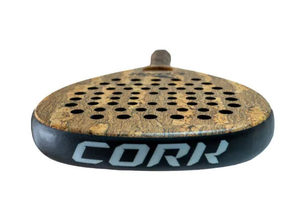 A close-up of the Cork Padel Premium Control II racket reveals a wooden pattern face and black edge. Cork is visible on the side. Several circular holes cover its surface, designed for precision by advanced players, as the handle extends away from view.