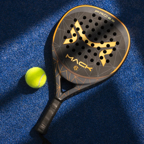 The Mack Pro 2.0 2024 Black padel racket by Mack Starke, showcasing a teardrop shape and sleek black and gold design with EVA Black Soft technology, elegantly rests on a blue surface next to a yellow tennis ball.