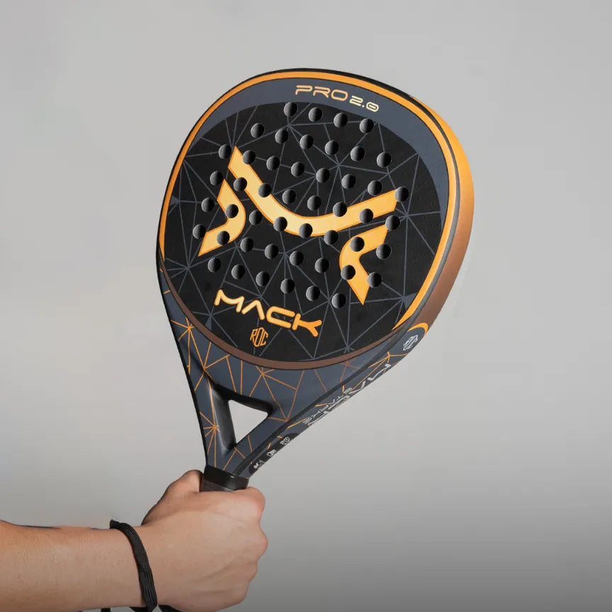 A person holds a teardrop-shaped racket displaying a sleek black and orange design branded with Mack Starke. The Mack Pro 2.0 2024 Black model has evenly spaced circular holes on its face, against a plain light gray background.
