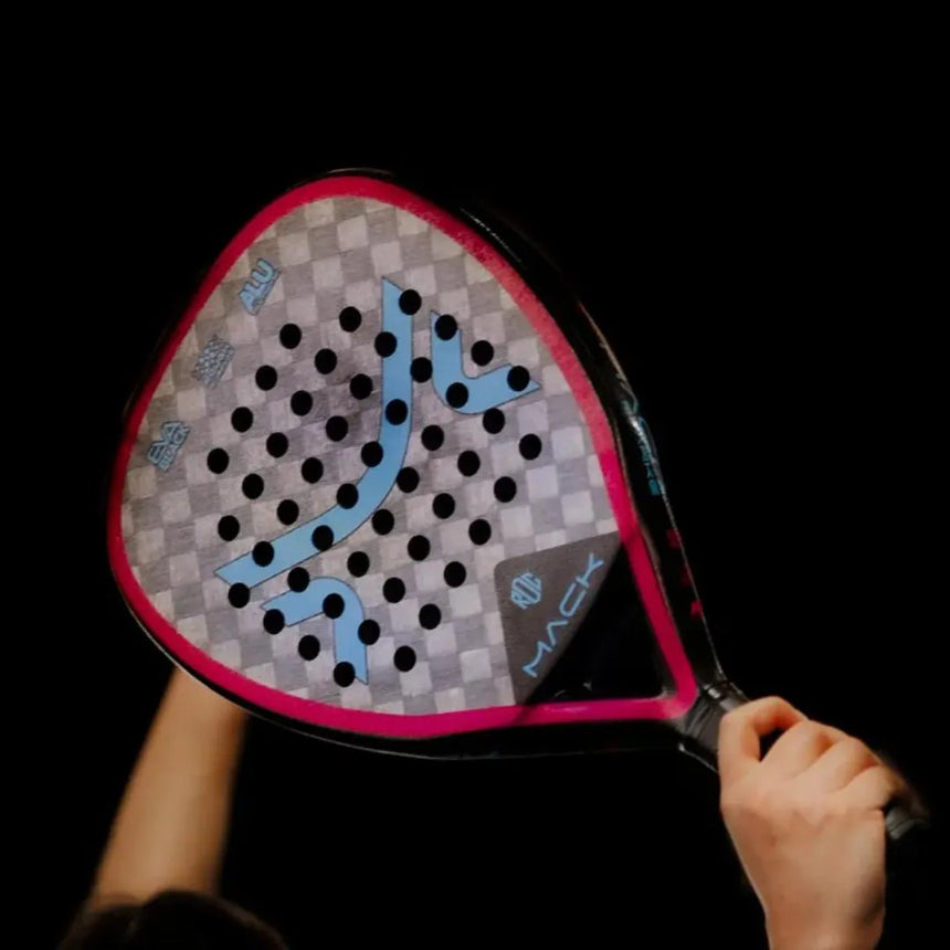 Close-up of hands holding the Mack Starke I-Pro Titanium 2024 padel racket against a black backdrop, featuring a diamond shape, Black Soft EVA rubber, pink frame, and gray face with geometric design and small holes.