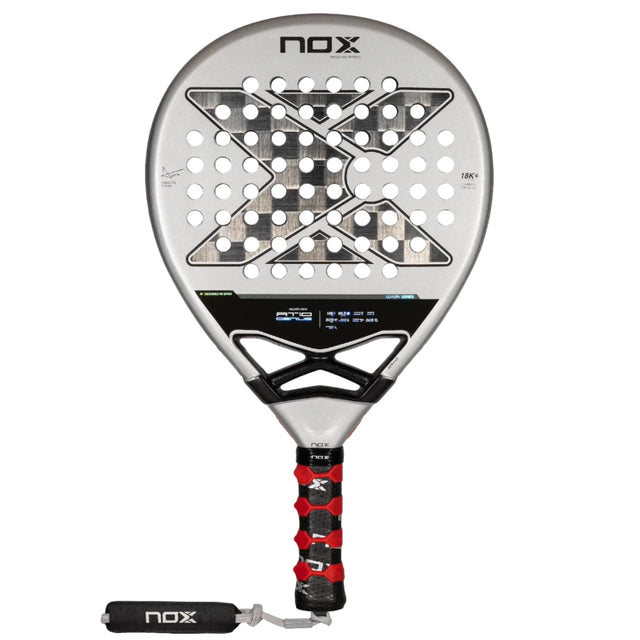 The NOX Padel Racket AT10 Genius 18K by 2024 Agustin Tapia, crafted from aluminized carbon fiber, features a silver design with a black grip and red accents. Its face has a geometric pattern with round holes and NOX displayed top and bottom, enhanced by innovative EOS Flap technology.