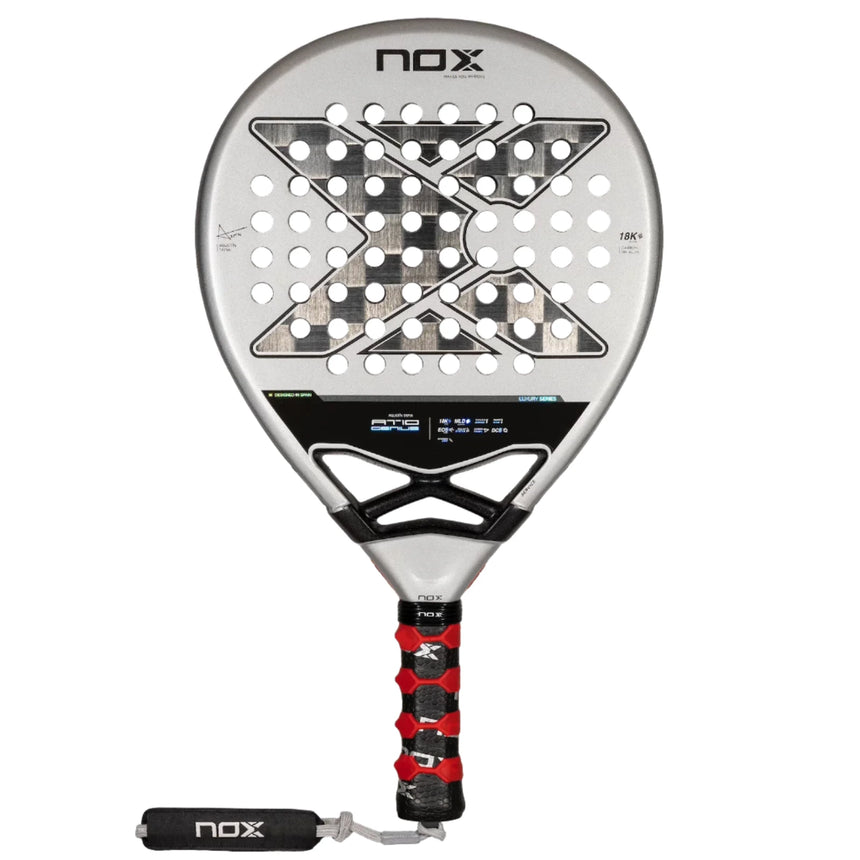 The NOX Padel Racket AT10 Genius 18K by 2024 Agustin Tapia, crafted from aluminized carbon fiber, features a silver design with a black grip and red accents. Its face has a geometric pattern with round holes and NOX displayed top and bottom, enhanced by innovative EOS Flap technology.