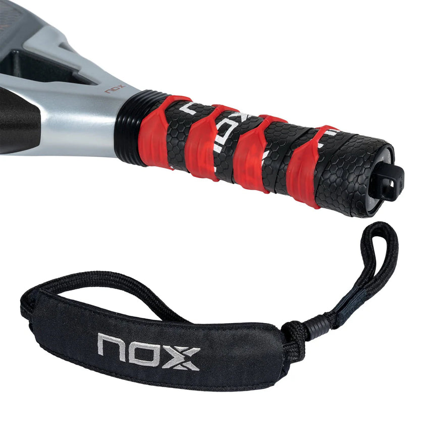 The NOX Padel Racket LA10 Future 2024 features a handle wrapped in black and red grip tape, highlighting the power of Aluminized 12K Carbon Fiber. A black strap with NOX in white offers a securing loop. This racket boasts a modern design with textured grip.