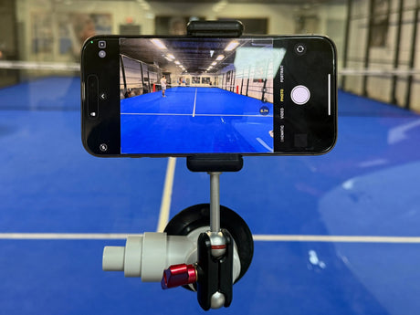 The Padel Smash Academys Padel Pro Mount secures a smartphone on a tripod, capturing the blue-floored indoor sports court with a net. The phones screen vividly displays this vibrant scene in the spacious, well-lit facility.