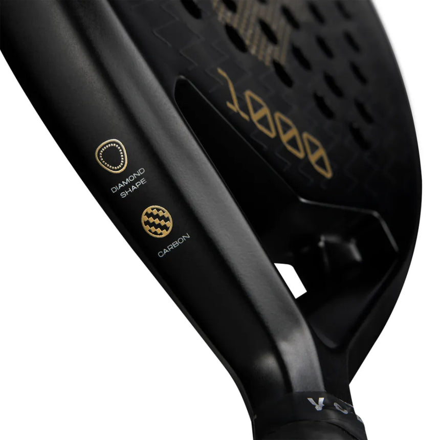 Close-up of the black VOLT 1000 v4 padel racket, showcasing gold 1000 text. Labels indicate a diamond shape and highlight its carbon structure with symbols. The textured surface adds an elegant touch.
