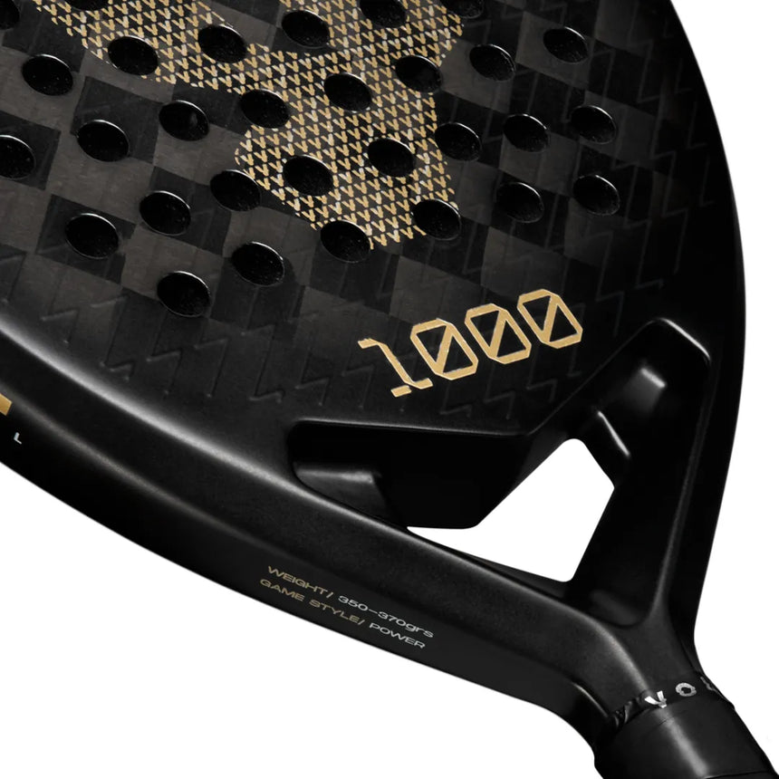 Close-up of a black VOLT 1000 v4 padel racket by Volt featuring a gold geometric pattern and 1000 in gold. The carbon structure provides strength, while the handle shows weight and game style. Surface adorned with multiple circular holes.