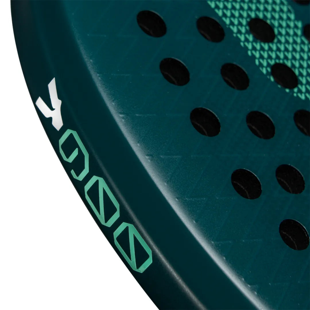 A close-up of a teal VOLT 900 v4 padel racket showcases small round holes and geometric edge designs. Its textured surface features green and white symbols near the handle, crafted from durable 3K Carbon Structure.