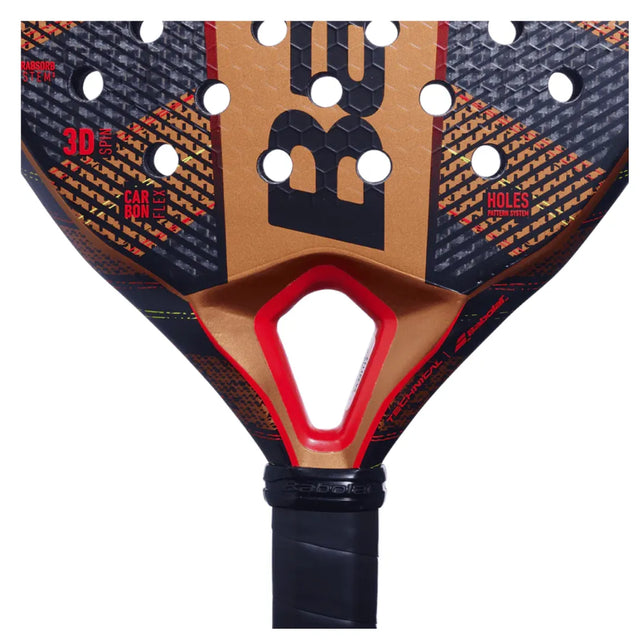 Close-up of the Babolat Technical Veron 2024 Padel Racket in black and dark orange. This like-new racket showcases a design with holes, textured patterns, and CARBON FLEX technology. The word carbon is prominent among branding elements, with a black taped handle for grip.