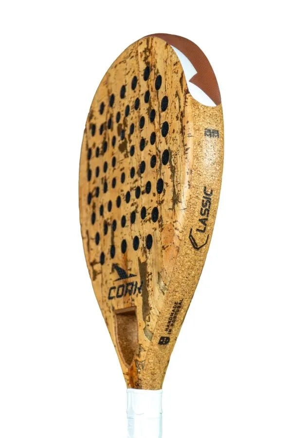 Meet the Cork Padel Classic by Cork Padel, crafted for comfort and control. It features an innovative drilling pattern and a cork-textured surface with round holes. A white grip-taped handle enhances the Classic branding set against its pristine white design.