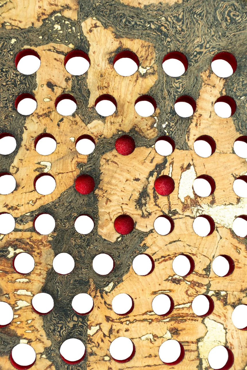 The Cork Padel Extreme Red by Cork Padel features a limited edition design with a textured surface and irregular circular cutouts. Some circles contain red spheres, set against a beige and dark swirled pattern resembling wood grain or marble.