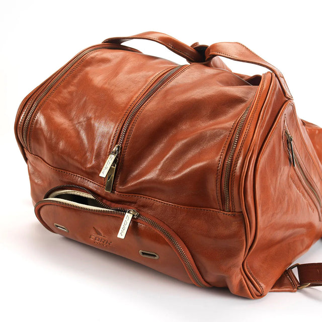 A brown genuine leather Cork Padel Thermobag with silver zippers and multiple compartments is shown. It has a smooth texture and is slightly open, revealing the interior lining. The embossed brand logo marks it as an exclusive Portuguese piece.