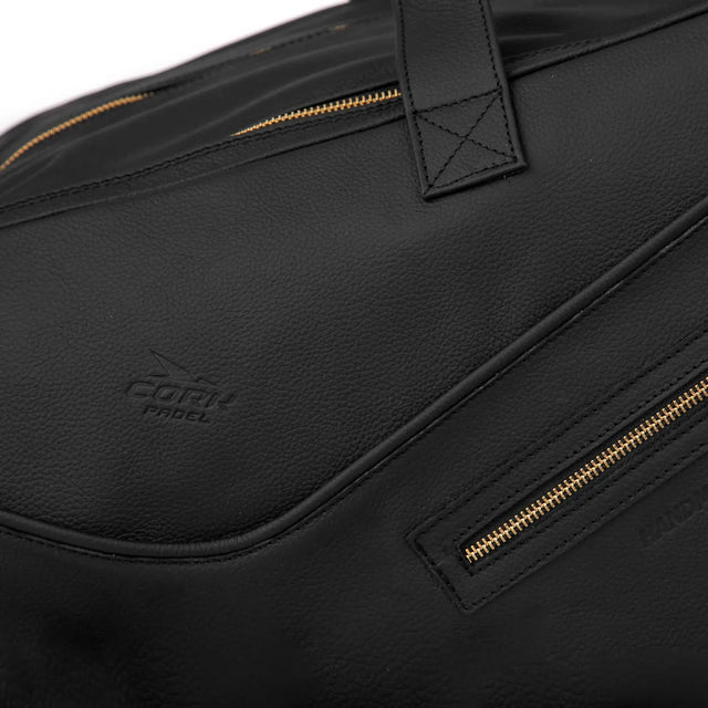 Close-up of the Cork Padels exclusive Cork Padel Leather Thermobag, a Portuguese black leather bag with gold zippers and an embossed logo. Its textured genuine leather boasts fine stitching near the handle and zippers, adding elegance to this premium accessory.