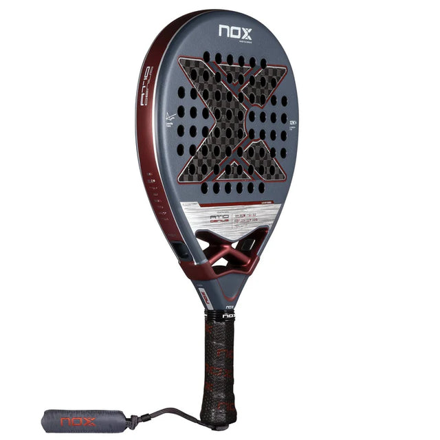The NOX Padel Racket AT10 Genius 12K by Agustin Tapia 2025 features a dark gray frame with a prominent X design, 12K carbon construction for precision and power, maroon edges, multiple holes, a black textured-grip handle, and a wrist strap labeled NOX.