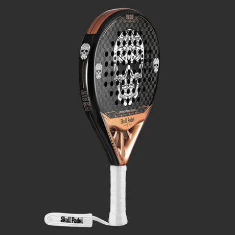 The SKULL PADEL V600 - 12K COPPER SKULL racket offers a sleek black and copper design with a bold large skull made of smaller skulls. Made from carbon fiber for intermediate players, it features a white grip and Skull Padel wrist strap, with V600 on the side against a dark gray background.
