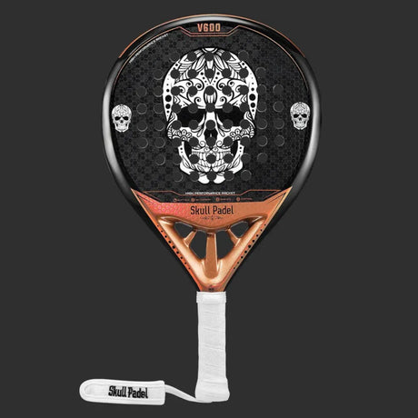 The SKULL PADEL V600 - 12K COPPER SKULL (LIKE NEW) is ideal for intermediate players, featuring a black and copper design with a central large white skull and smaller ones on the sides. Its crafted from carbon fiber, with a white grip tape on the handle, showcasing Skull Padel on the wrist strap.