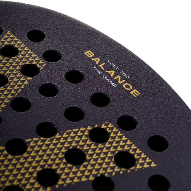 Close-up of the VOLT 700 v4 padel racket by Volt, featuring a black design with round holes and Balance The Game in yellow near the edge. It has a textured patterned surface and a 3K carbon structure that improves performance with flexible shock absorption technology.