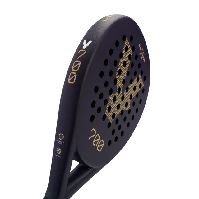 Close-up of the VOLT 700 v4 padel racket by Volt, featuring gold accents and branding. Its 3K carbon structure offers a textured face, while flexible shock absorption tech boosts play. The handle is subtly detailed, with 700 and symbols edging the refined design.